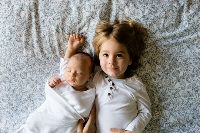 Грудной ребенок и девочка лежат вместе на кровати